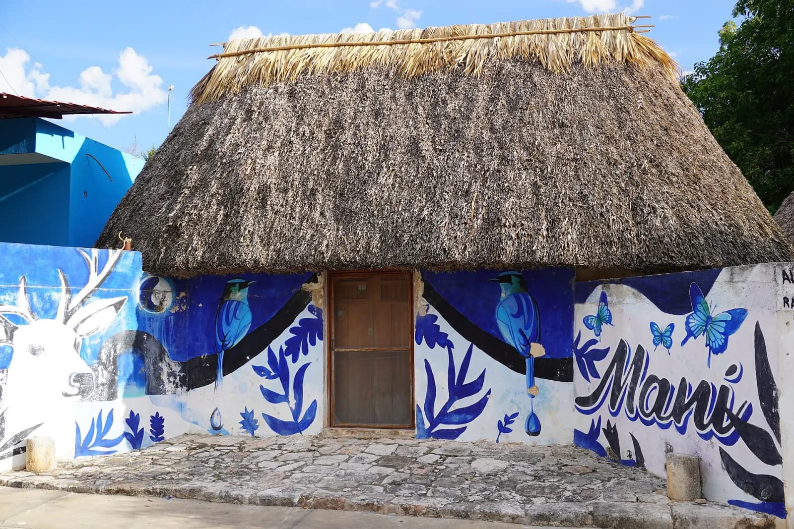 Casa maya con techo de huano y mural azul con la palabra Maní, en Yucatán