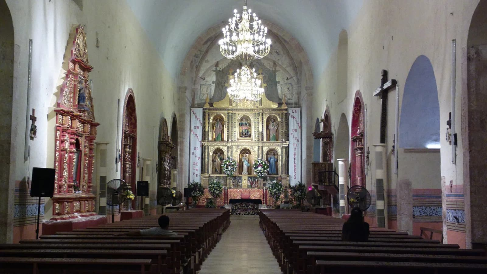 Nave de la iglesia de San Miguel Arcángel en Maní con retablos dorados y candiles encendidos