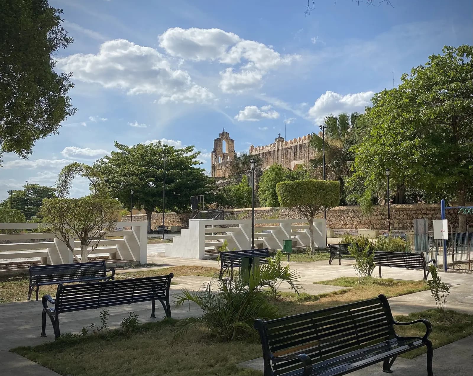 Bancas y jardín del parque de Maní con la espadaña del exconvento al fondo