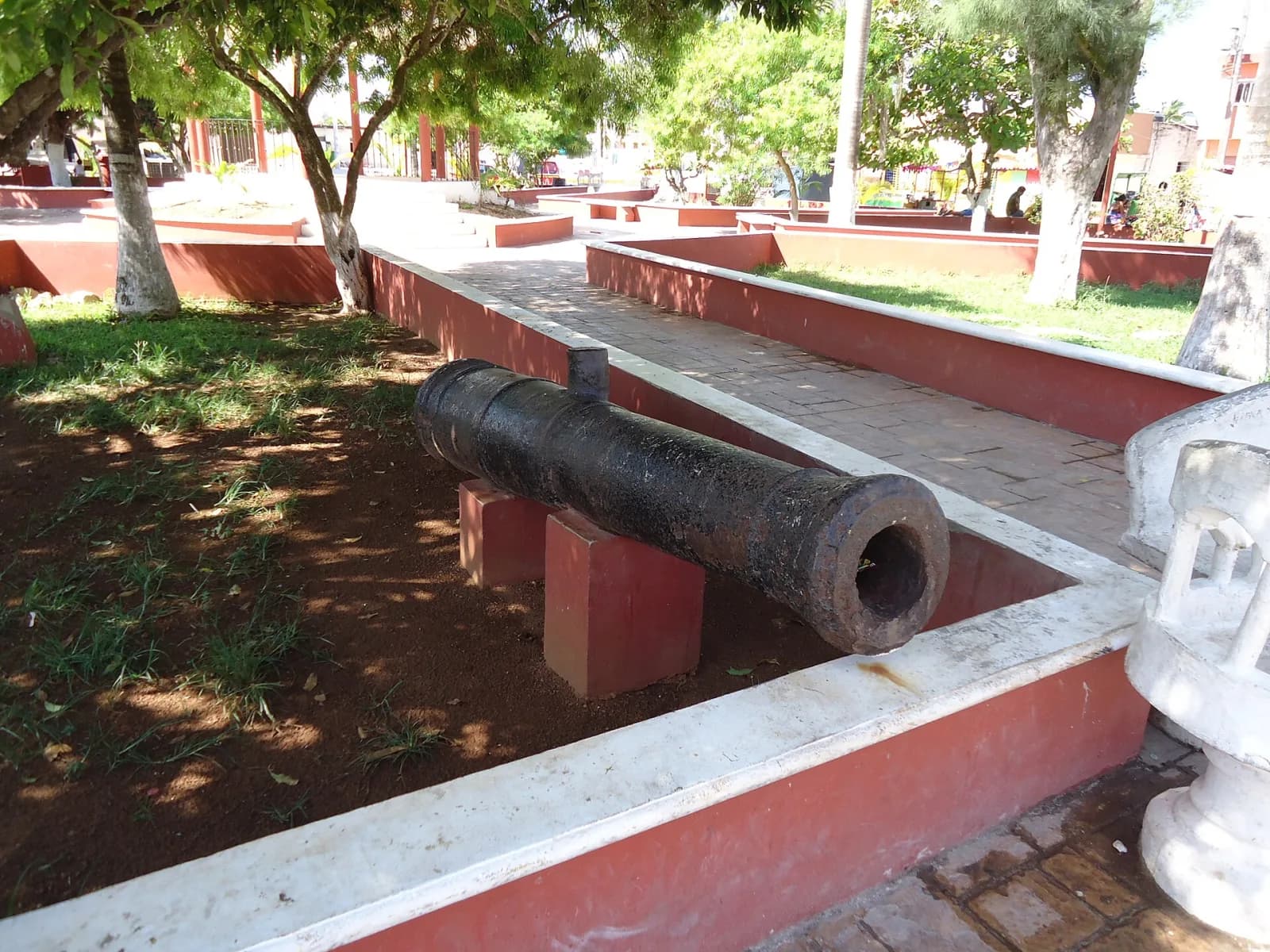 Cañón antiguo exhibido entre jardineras en el parque principal de Sisal, Yucatán