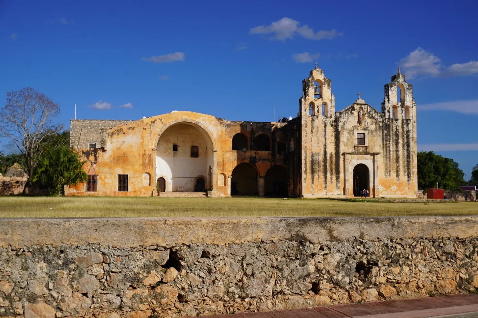 Exconvento de San Miguel Arcángel en Maní visto detrás de un muro de piedra, bajo cielo azul