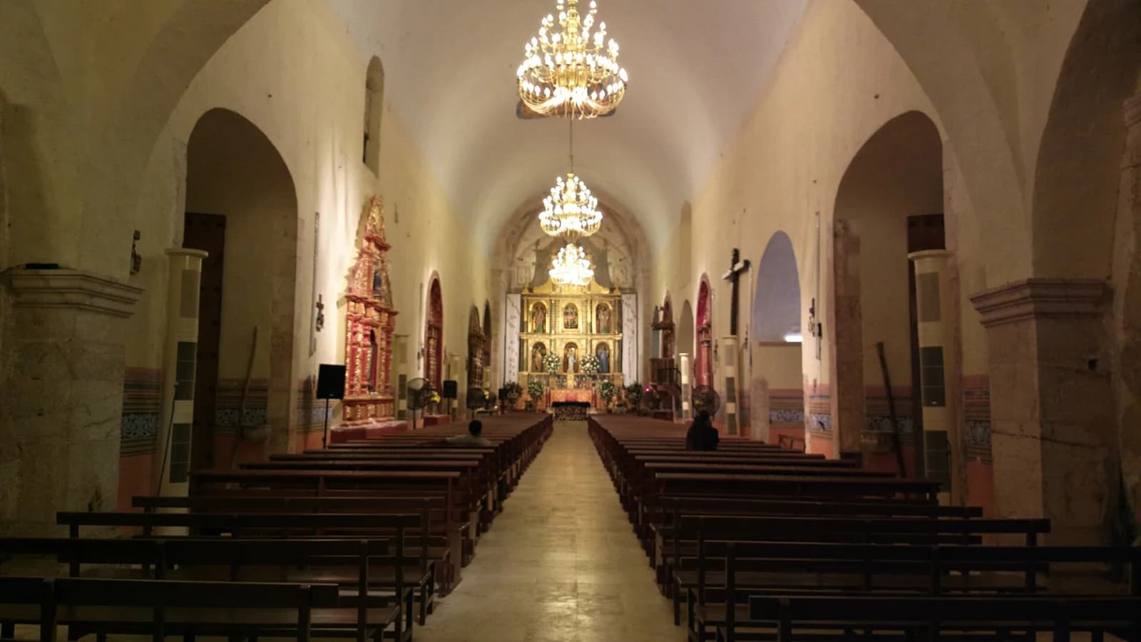 Interior de la iglesia de San Miguel Arcángel en Maní de noche, con bancas y el retablo mayor al fondo