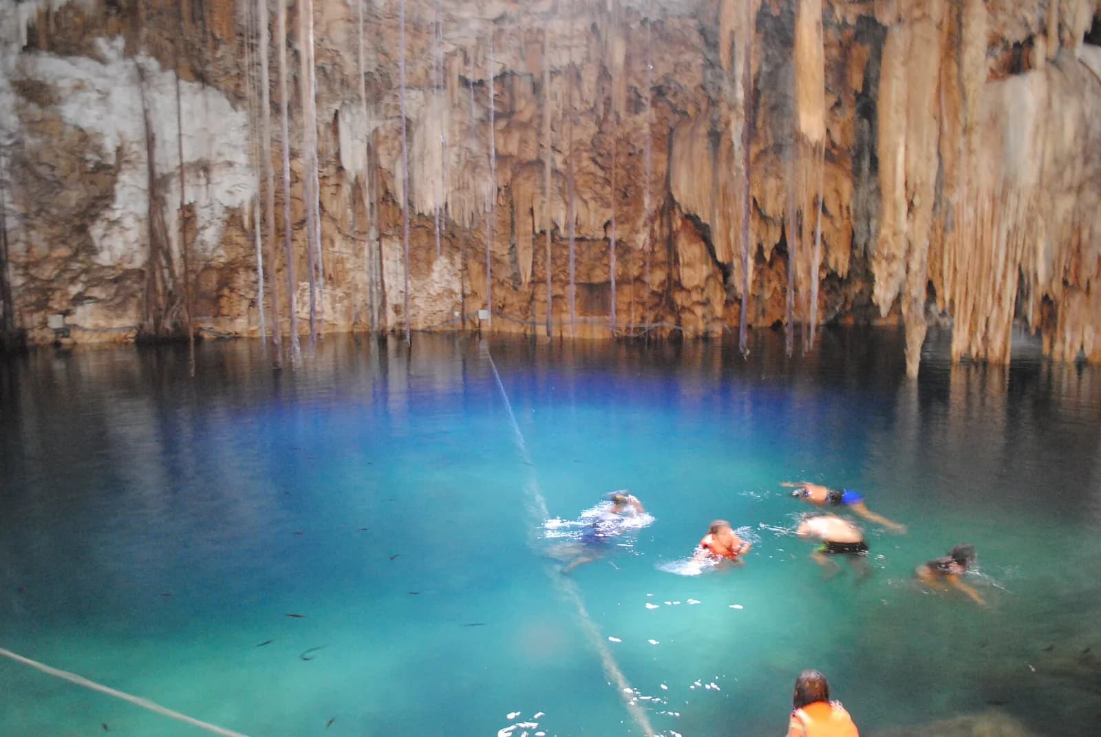 Nadadores en el agua clara del cenote X’kekén bajo paredes de roca, Dzitnup, Valladolid