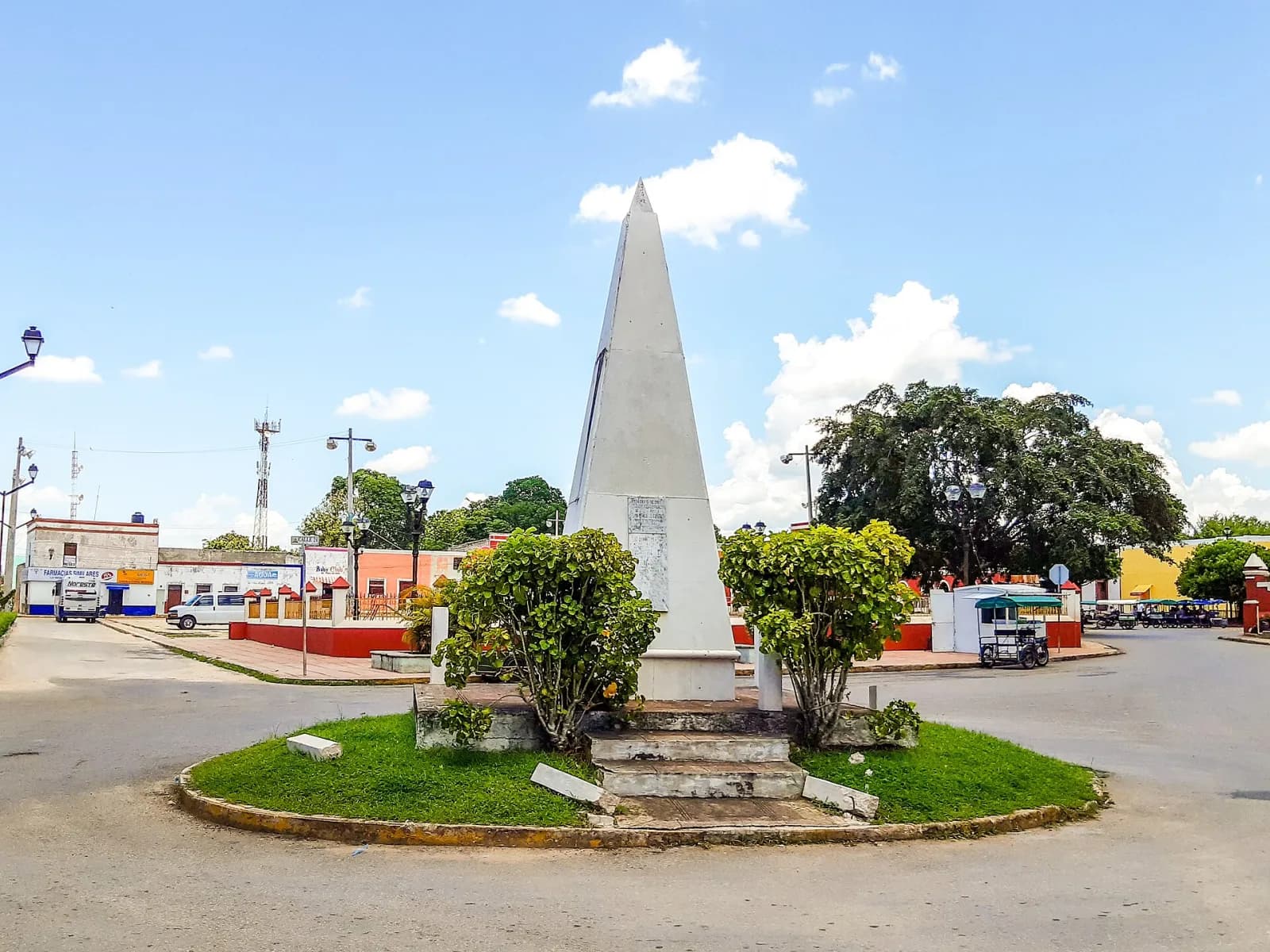 Obelisco blanco de los Quince Grandes en Espita, Yucatán, rodeado de arbustos bajo cielo azul